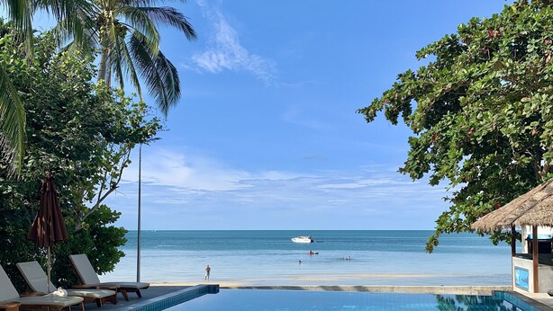 Piscina infinita azul límpida com espreguiçadeiras e vista para a praia e o oceano.