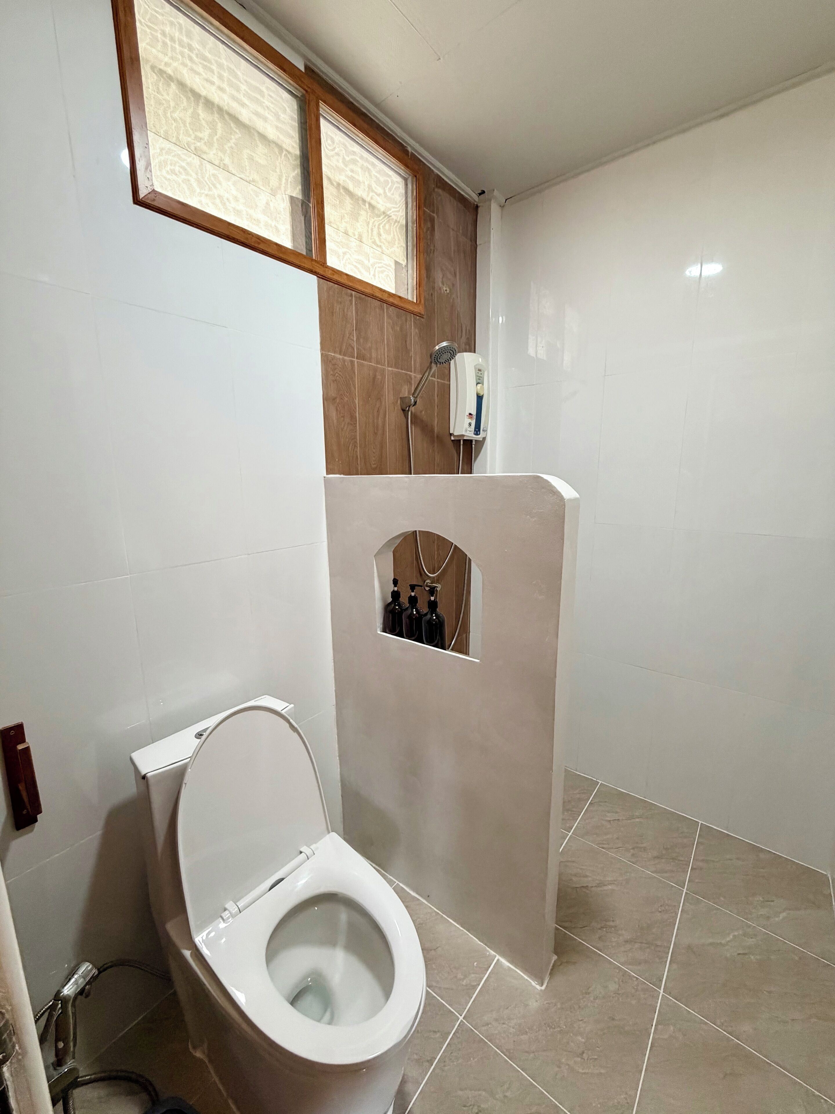 A bathroom with a toilet, a shower, and a window.