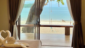 Quarto com cama grande, vista para a praia e uma árvore na janela.