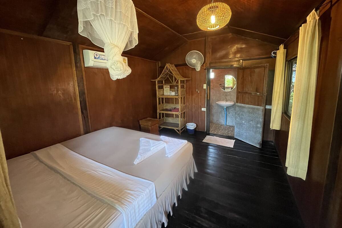 Una habitación con cama, ventilador, estante con cestas, espejo y puerta que da al exterior.