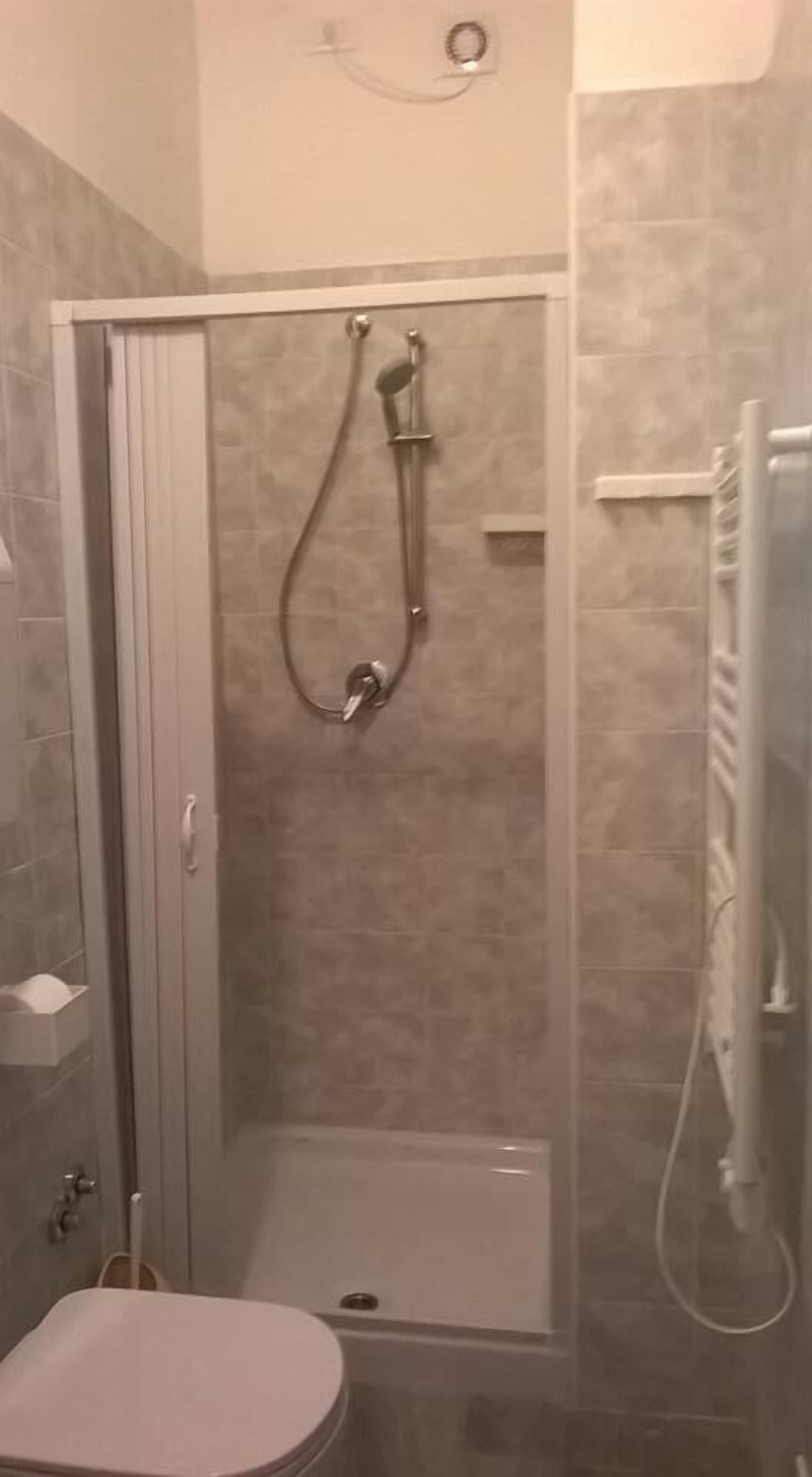 A small, enclosed shower stall with a glass door, a toilet, and a towel rack.