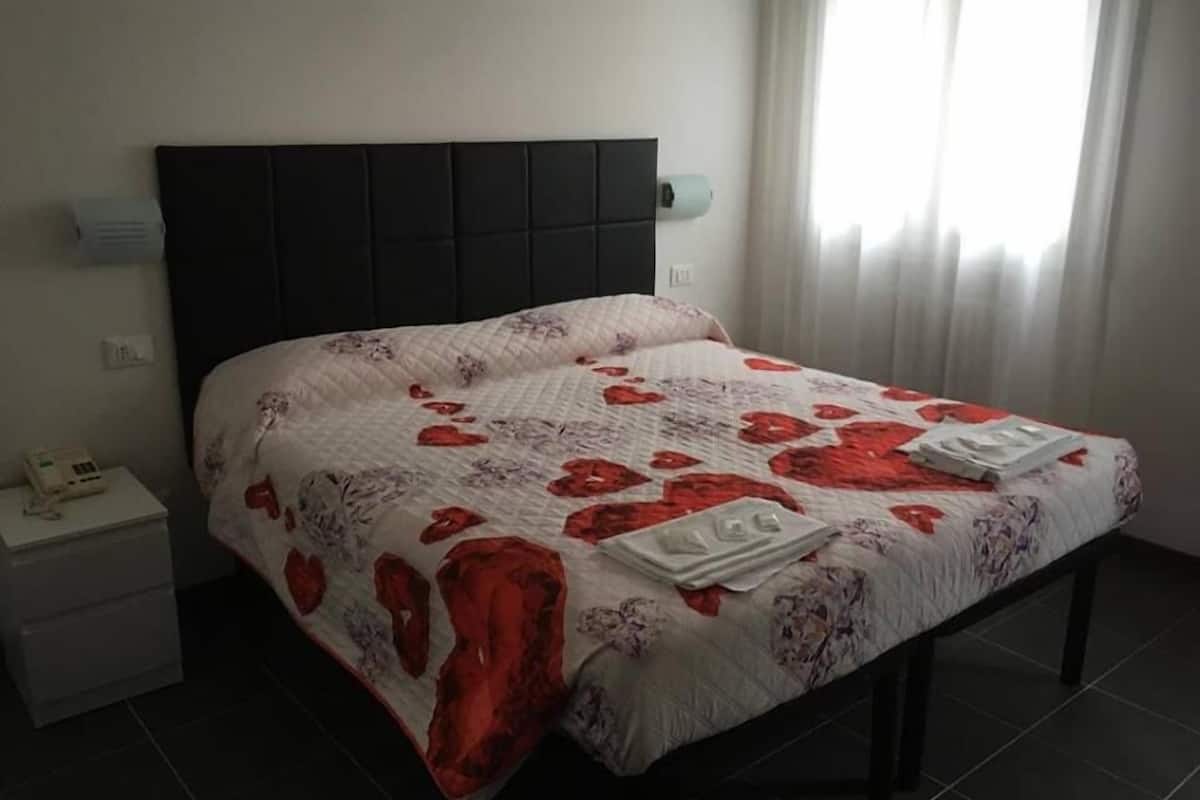 Una cama bien hecha con un edredón estampado de flores y dos toallas dobladas con cuidado.
