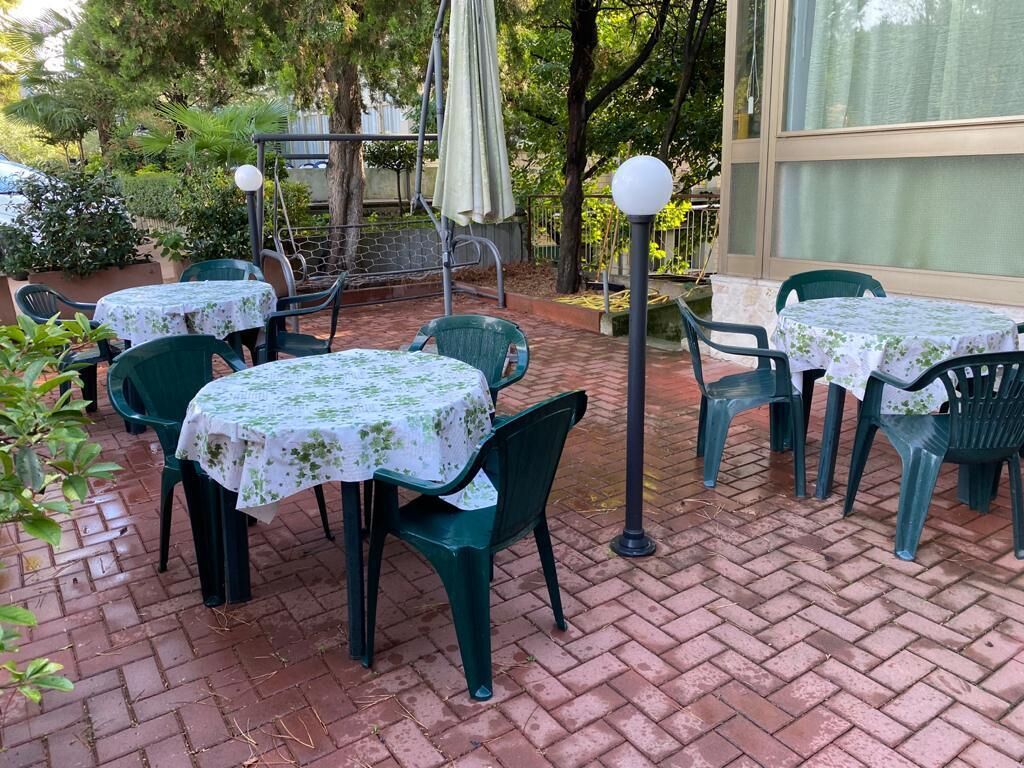 Une terrasse extérieure avec des tables et des chaises, entourée de verdure et dotée d’un sol en briques.