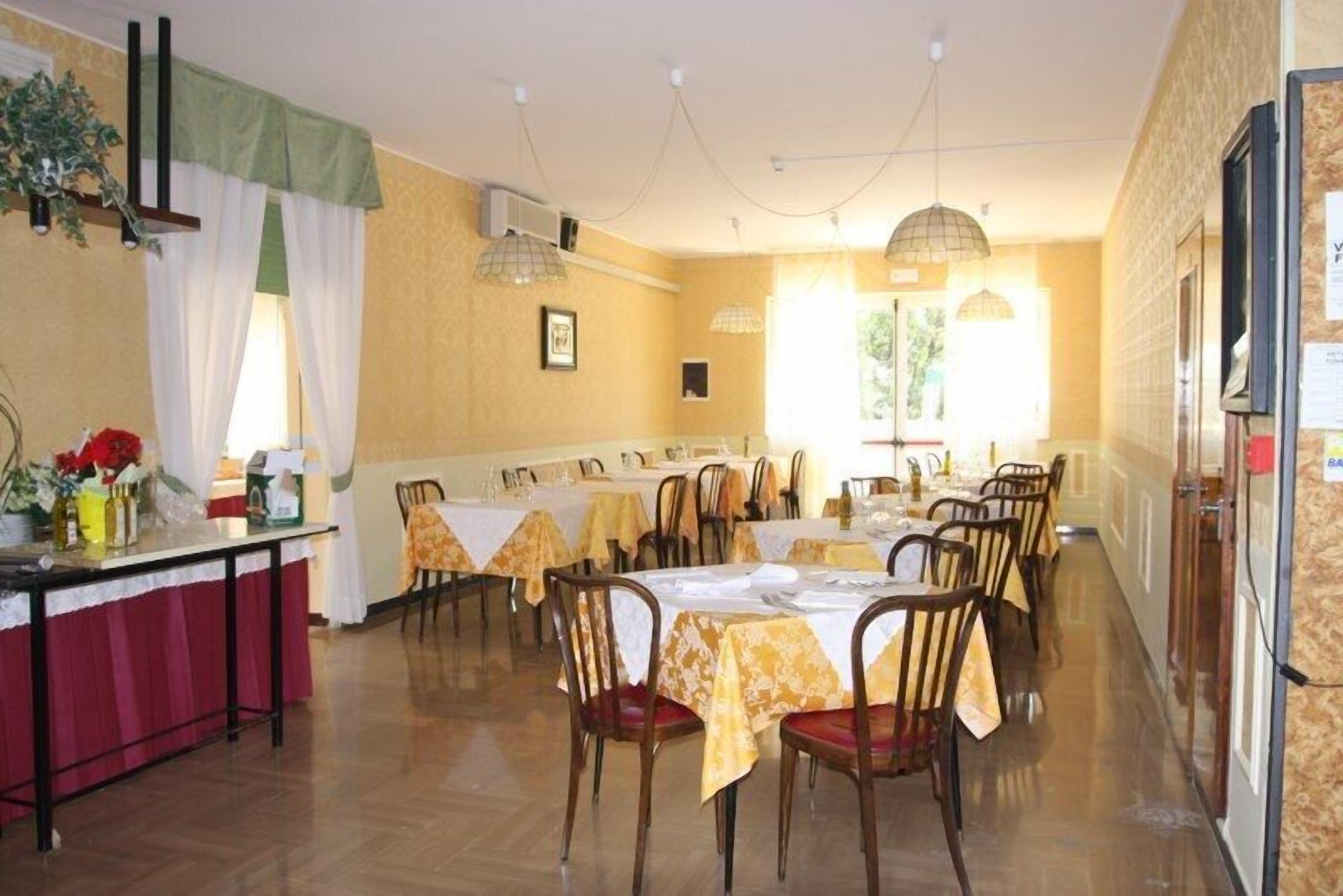 A dining area with multiple tables and chairs, a counter with a red tablecloth, and a window with curtains.