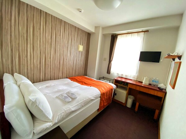 A hotel room with a bed, a desk, a chair, a TV, and a window with curtains.