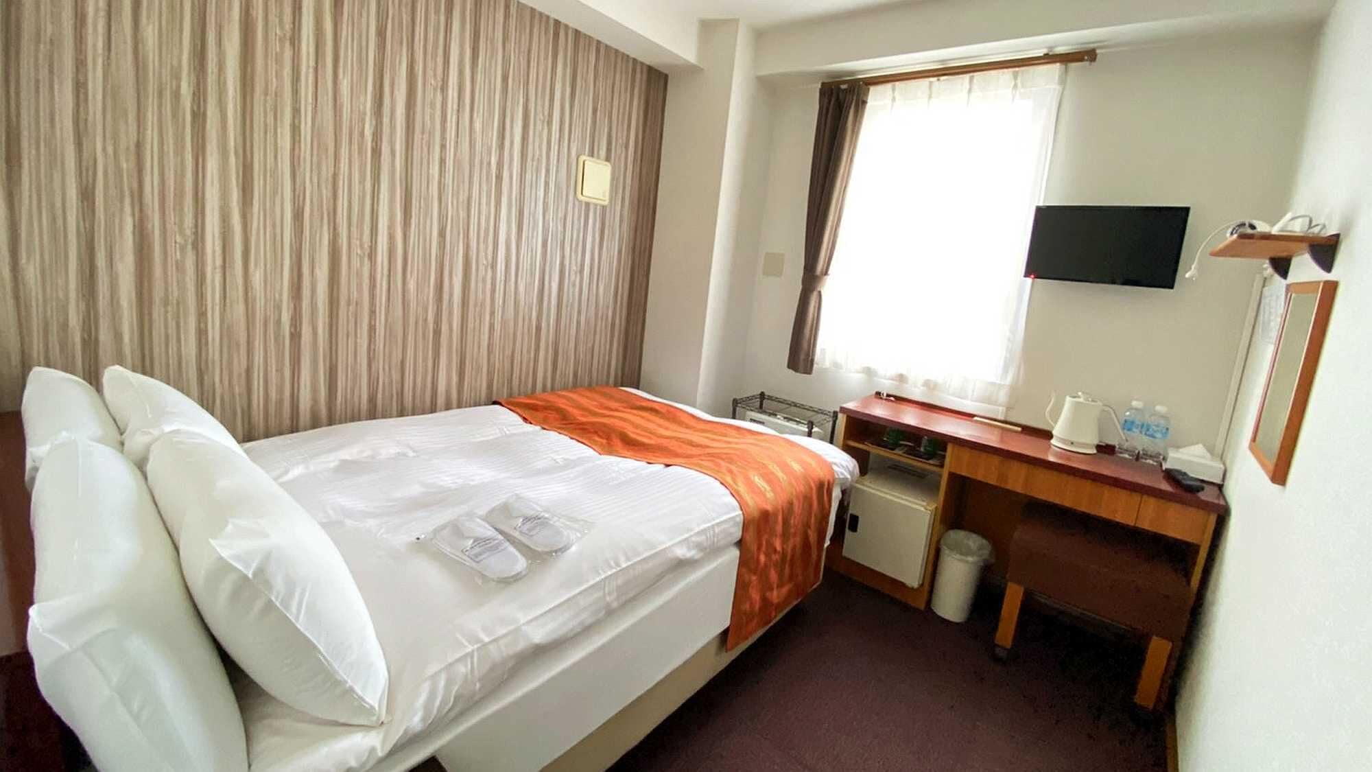 A hotel room with a bed, a desk, a chair, a television, and a window.