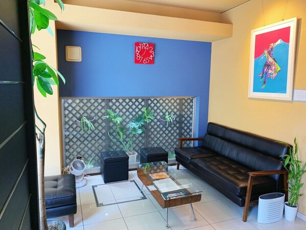 A modern living room with a blue accent wall, a black leather sofa, a glass coffee table, and a decorative clock. - Web Hotel Tokyo Asakusabashi (Tokyo)