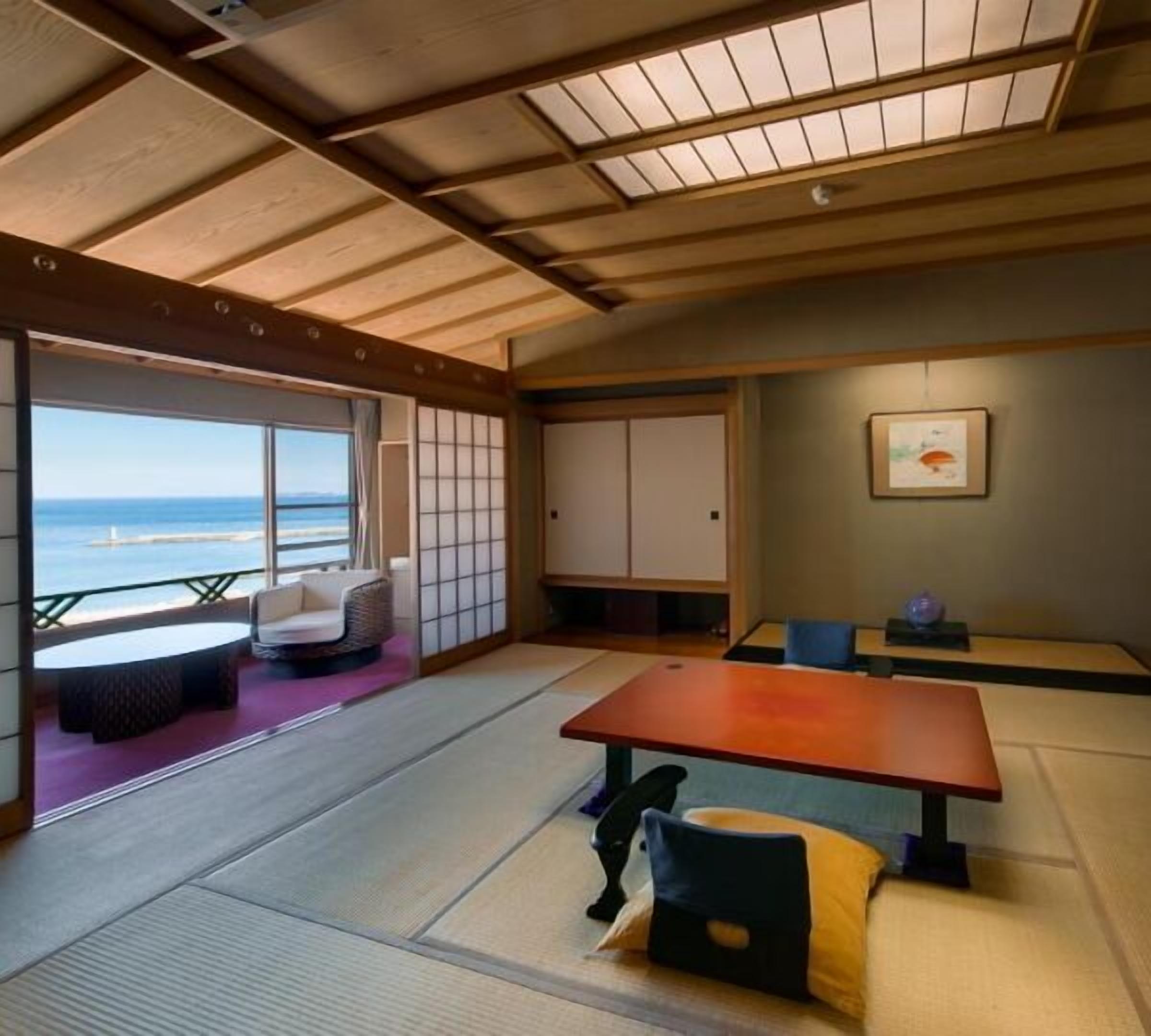 Une pièce avec un sol recouvert de tatamis, offrant une vue sur la mer, comprenant une table en tatami et un canapé.