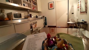 A modern kitchen with a microwave, oven, and a glass table with a bowl of colorful items. - Room Inn (Milan)