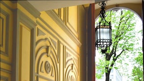 An ornate doorway with a wrought iron gate, a street view with a statue, and a tree visible through the archway. - Room Inn (Milan)