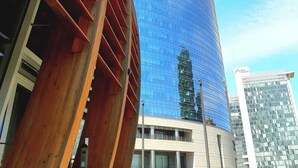 A modern high-rise building with a curved glass facade and a prominent red and white logo at the top. - Room Inn (Milan)