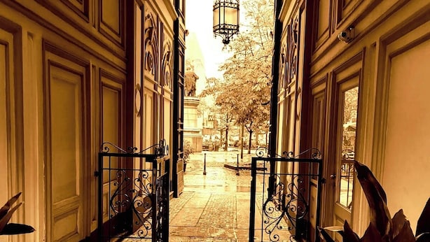 A corridor with ornate doors, a cobblestone floor, and a view of a statue and trees in the distance. - Room Inn (Milan)