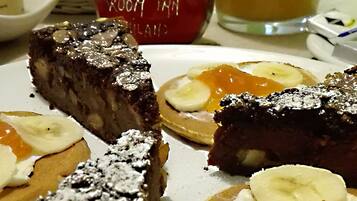 Una colazione con una fetta di torta, pancake guarniti con banane a fettine e panna montata, e un bicchiere di succo d'arancia.