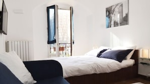 A modern hotel room with a bed, a sofa, a glass coffee table, and a window with curtains. - Room Inn (Milan)