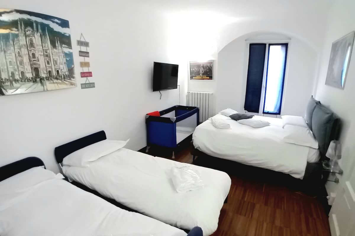 A hotel room with two single beds, a desk, a chair, a TV, and a window with curtains.