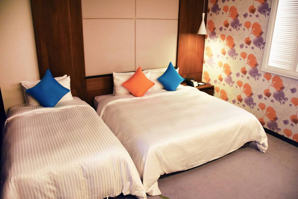 Habitación de hotel con dos camas, cada una con ropa de cama blanca y almohadas azules y anaranjadas.