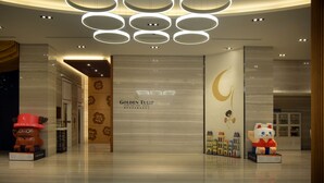 Een hotel lobby met een modern design, met een groot bord voor Golden Tulip, een decoratieve muur met bloemmotieven en een maanvormig ontwerp op de muur.