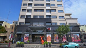 Een meerlaags hotel met een moderne gevel, een opvallende ingang en een groot bord waarop 