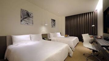 A hotel room with two beds, a desk, a chair, a lamp, and artwork on the walls.