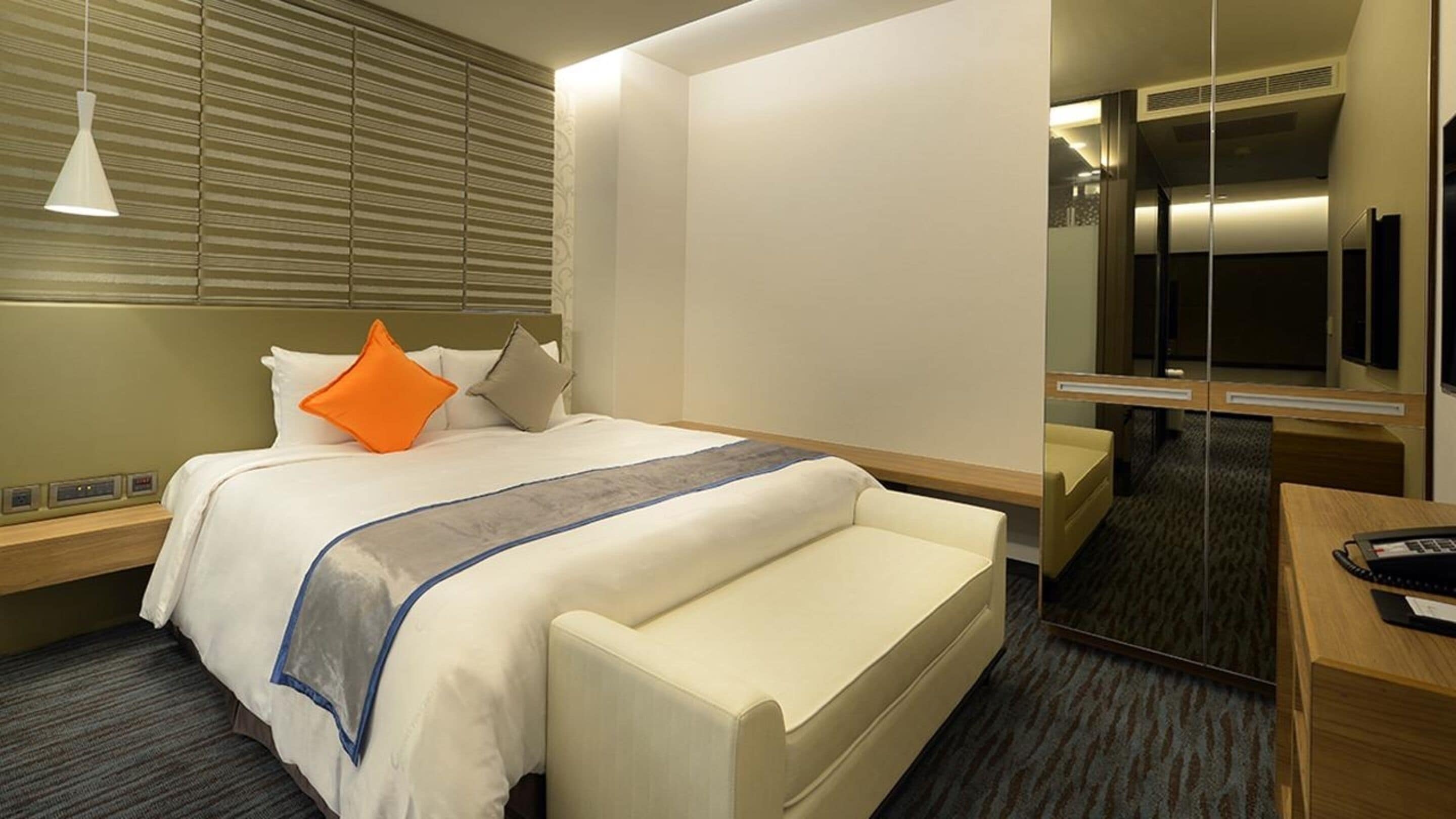 Una habitación de hotel con cama, mesitas de noche, escritorio, silla, espejo y teléfono.