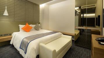 Una habitación de hotel con cama, mesitas de noche, escritorio, silla, espejo y teléfono.