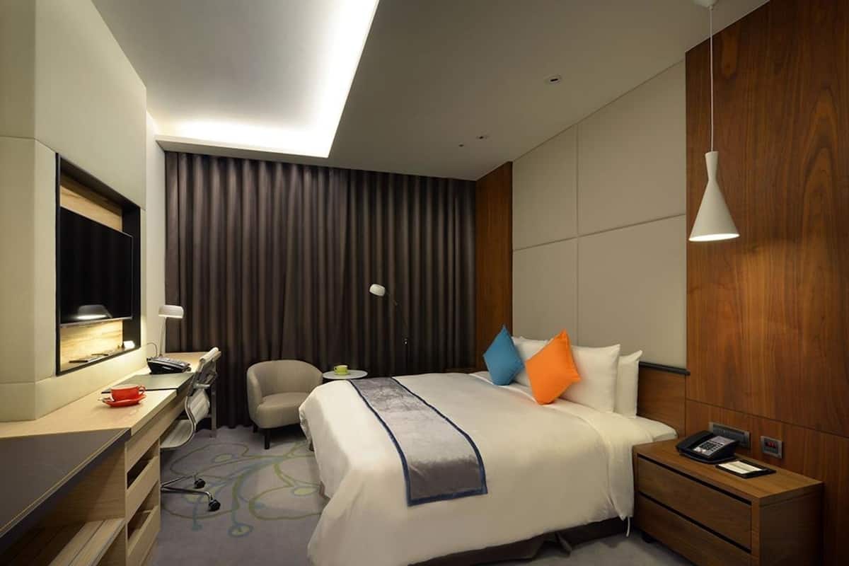 Habitación de hotel con cama, mesita de noche, escritorio, silla y un espejo grande.