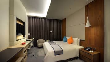A hotel room with a bed, bedside table, desk, chair, and a large mirror.