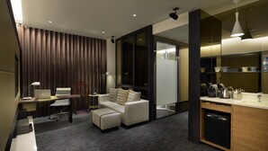 Een moderne hotelkamer met een bank, een bureau met een laptop, een koffiezetapparaat en een minibar.