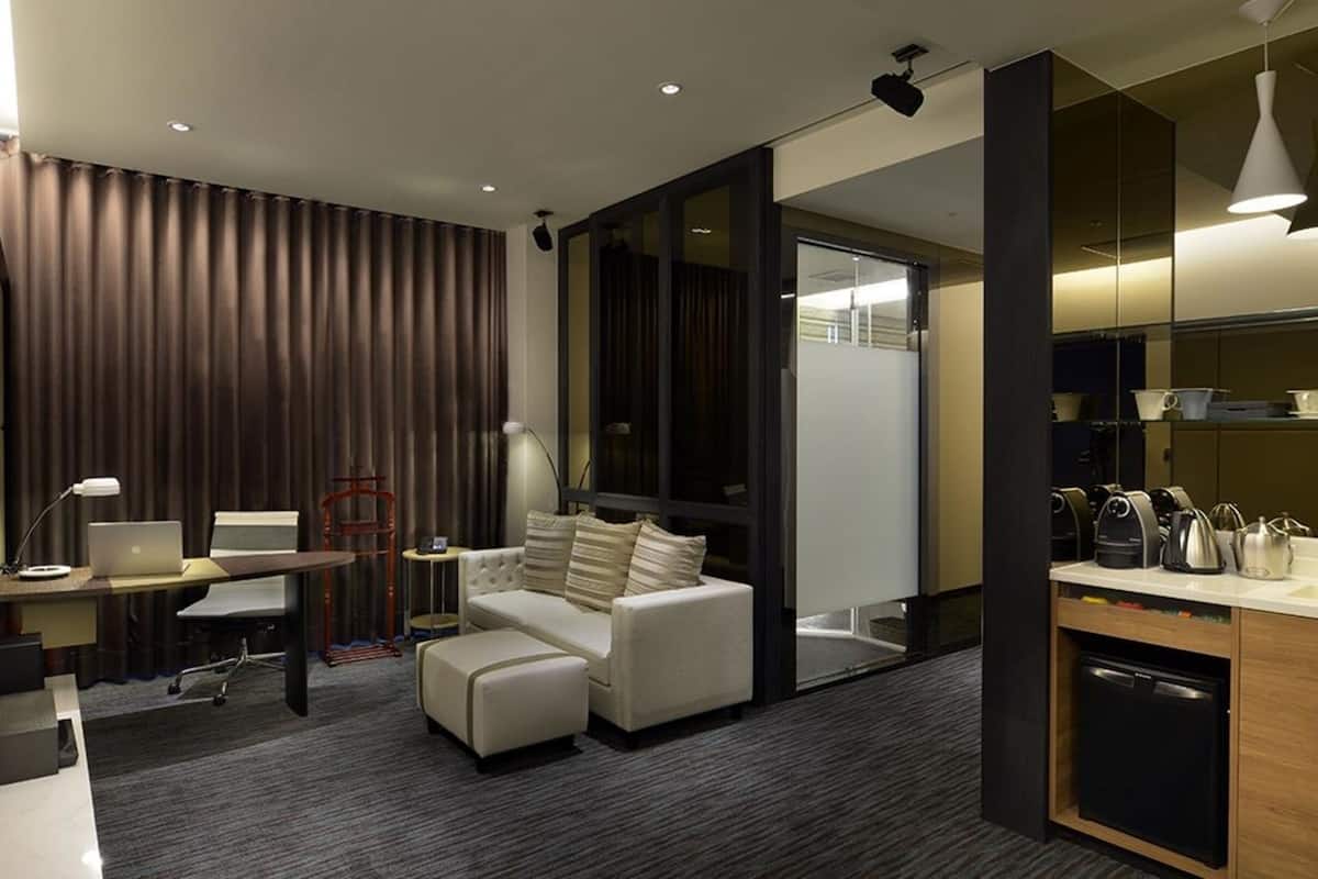 Una habitación de hotel moderna con sofá, escritorio, laptop, cafetera y mini refrigerador.