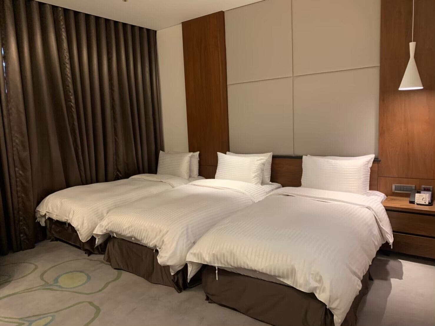 A hotel room with a large bed, a wooden headboard, a bedside table with a lamp, and a curtain on the window.