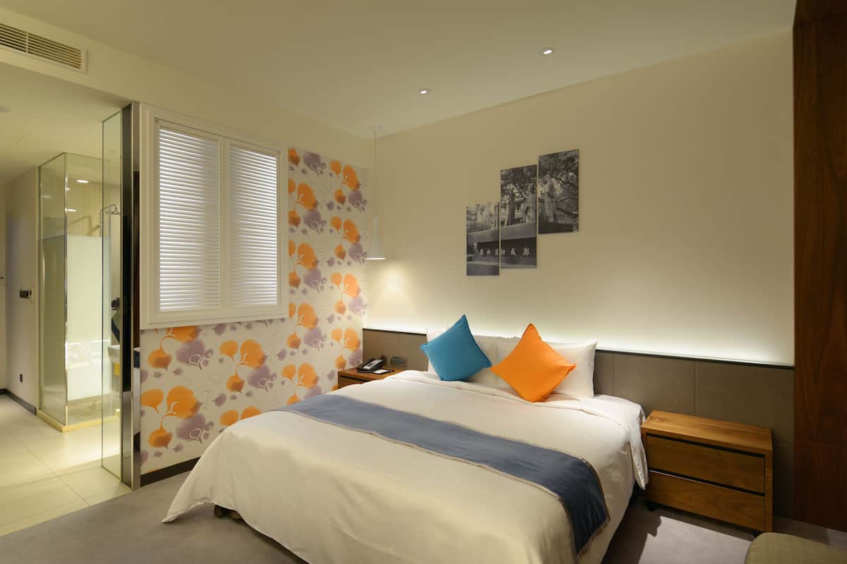 Un dormitorio moderno con cama, mesitas de noche, cabecera, mampara de cristal para la ducha y decoración en la pared.