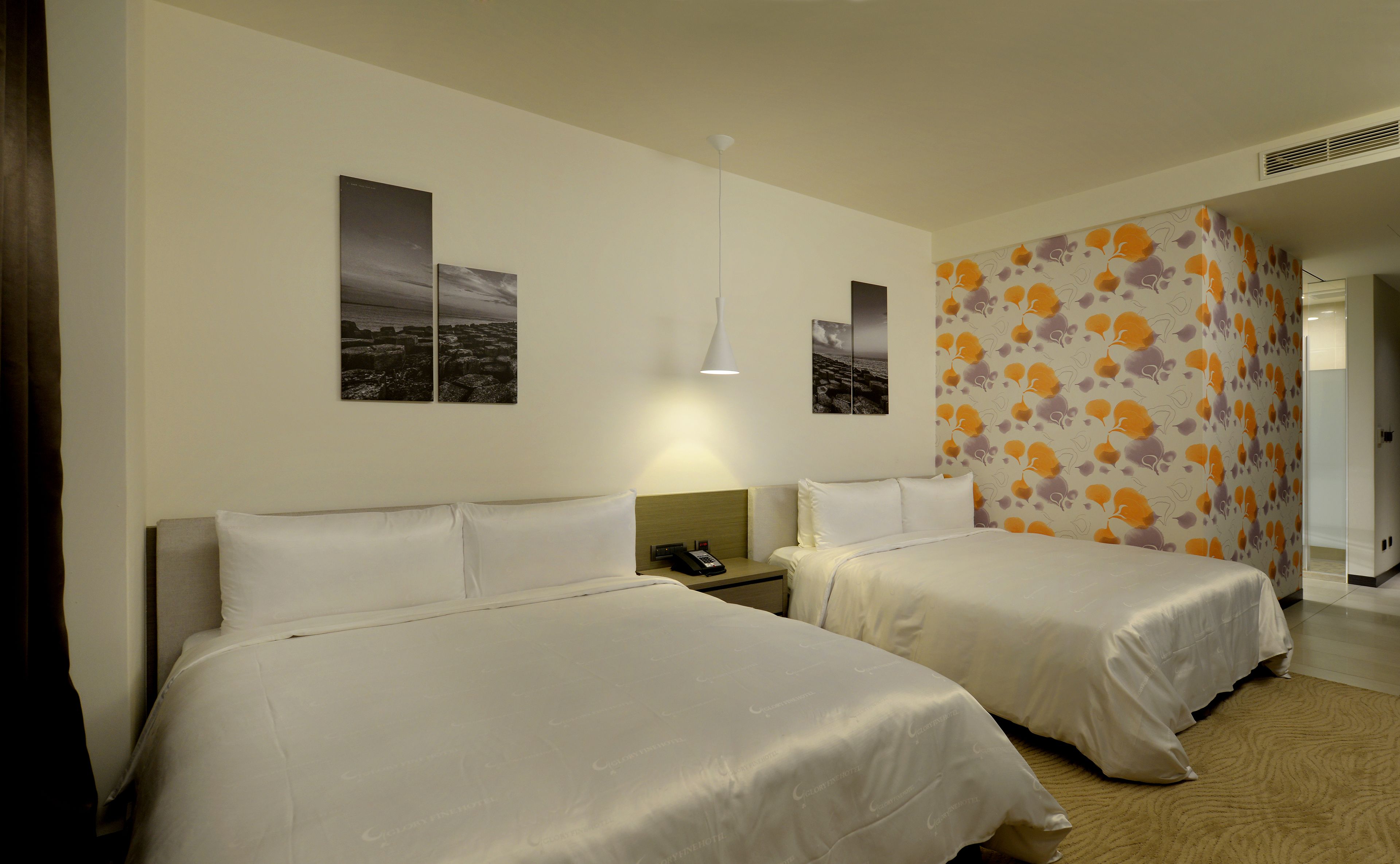 A hotel room with two beds, a nightstand, a lamp, and a wall with a floral pattern.