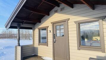 A small cabin with a wooden porch, a sliding door, and two windows.