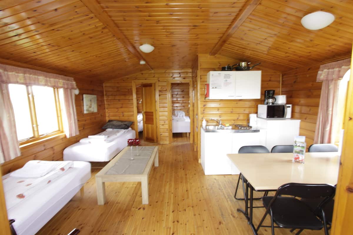 A cabin interior with wooden walls, a kitchenette, a dining area, and two beds.
