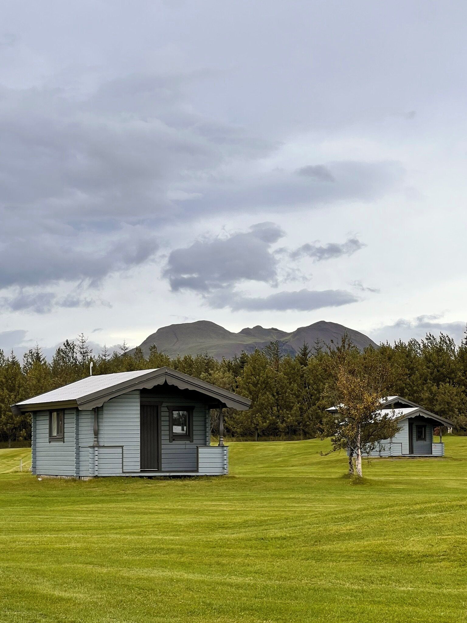 Deux petites cabanes, avec un champ verdoyant et des montagnes en arrière-plan.