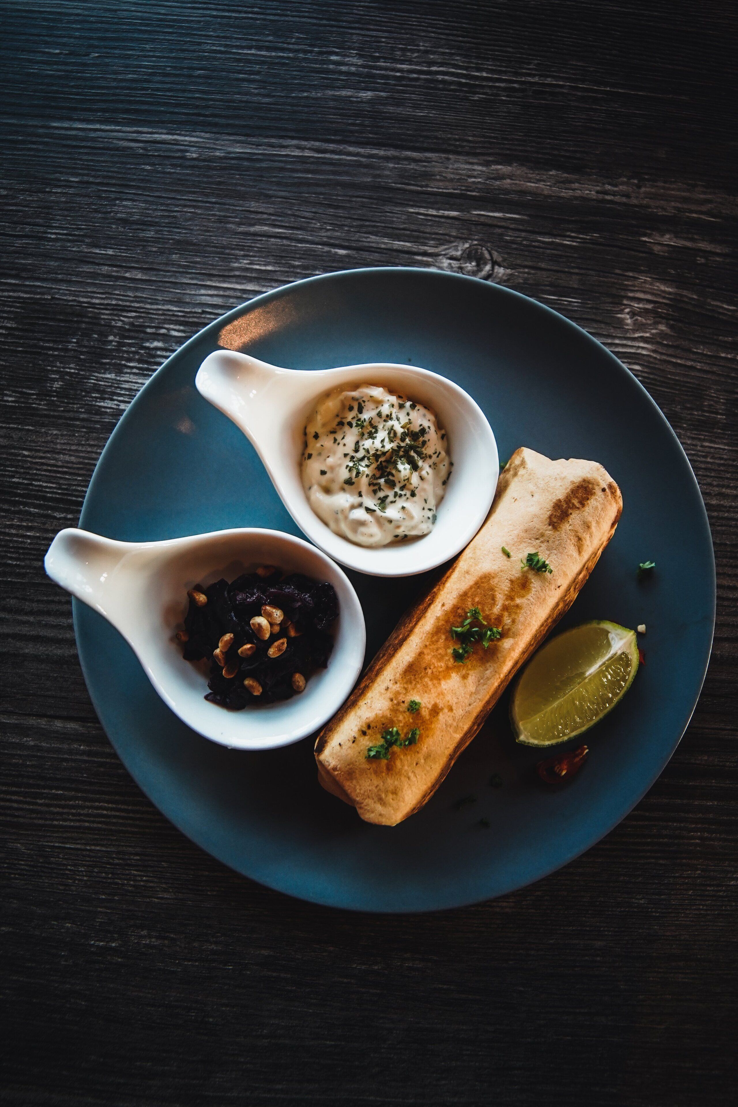 Une assiette avec un plat grillé, deux petits bols de sauces et un quartier de citron vert.