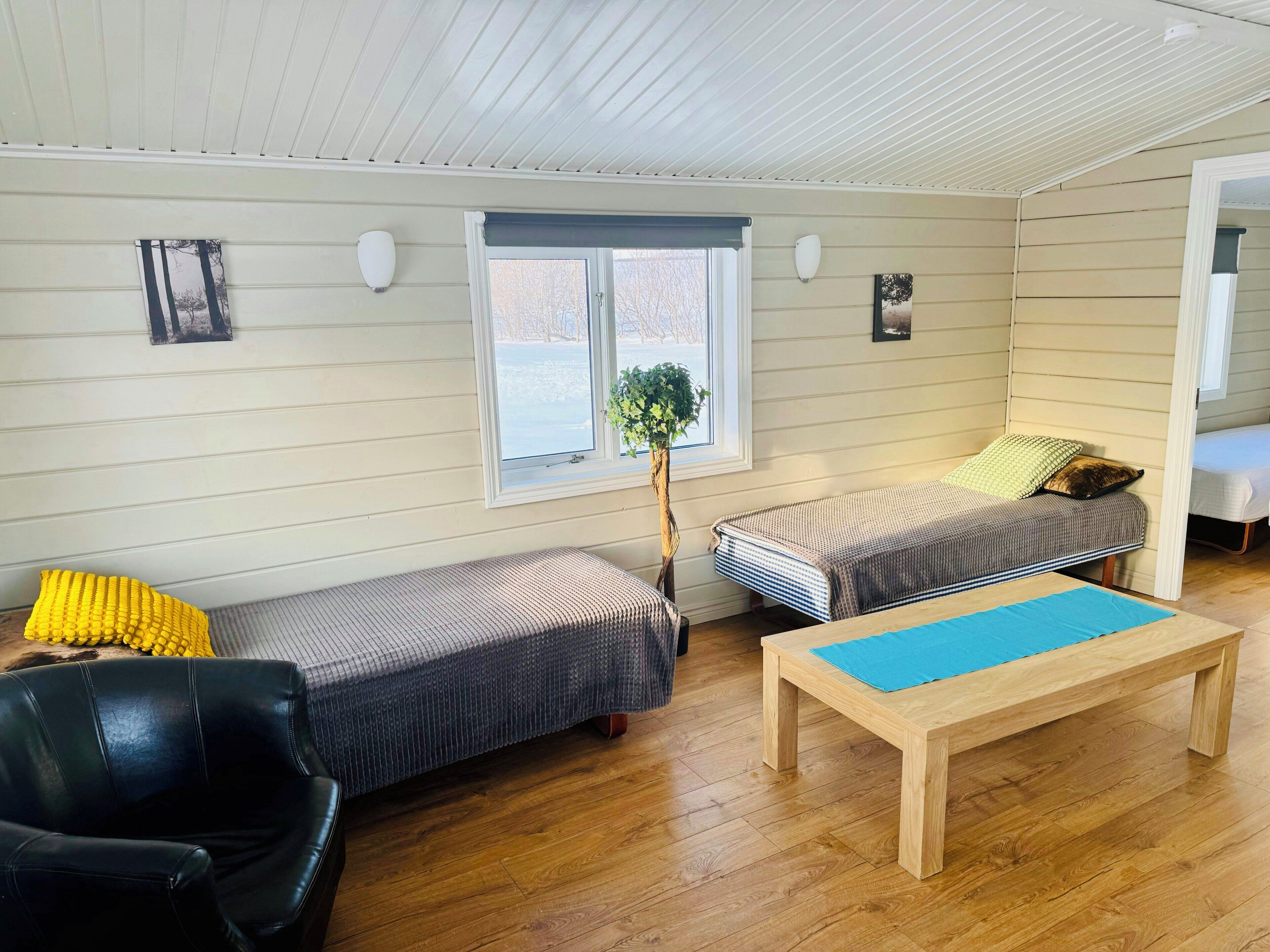 A room with two beds, a wooden bench, a chair, and a window with a view.