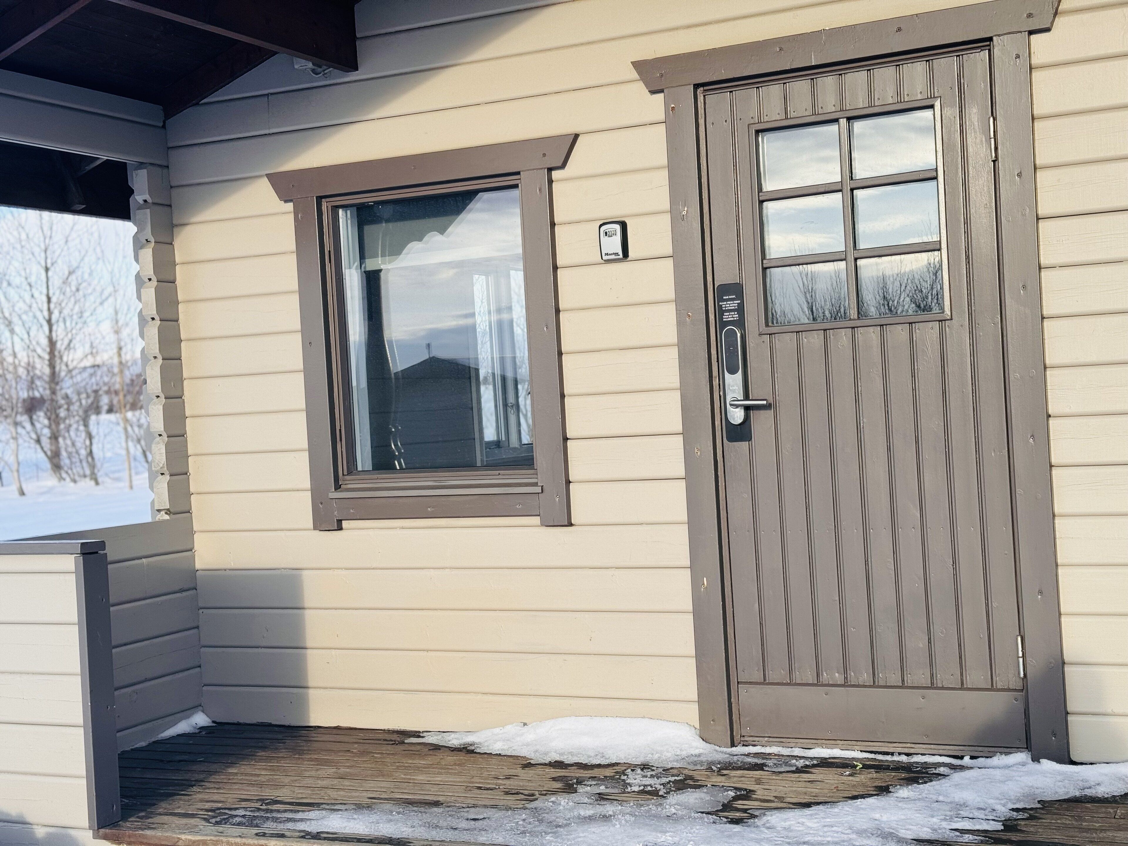 Uma casa bege com porta e janela marrons, um pequeno alpendre e neve no chão.
