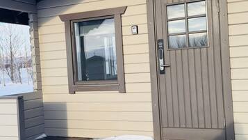 Uma casa bege com porta e janela marrons, um pequeno alpendre e neve no chão.