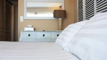 Een net opgemaakt bed met een gestreept dekbed, een nachtkastje met een lamp, en een spiegel aan de muur.