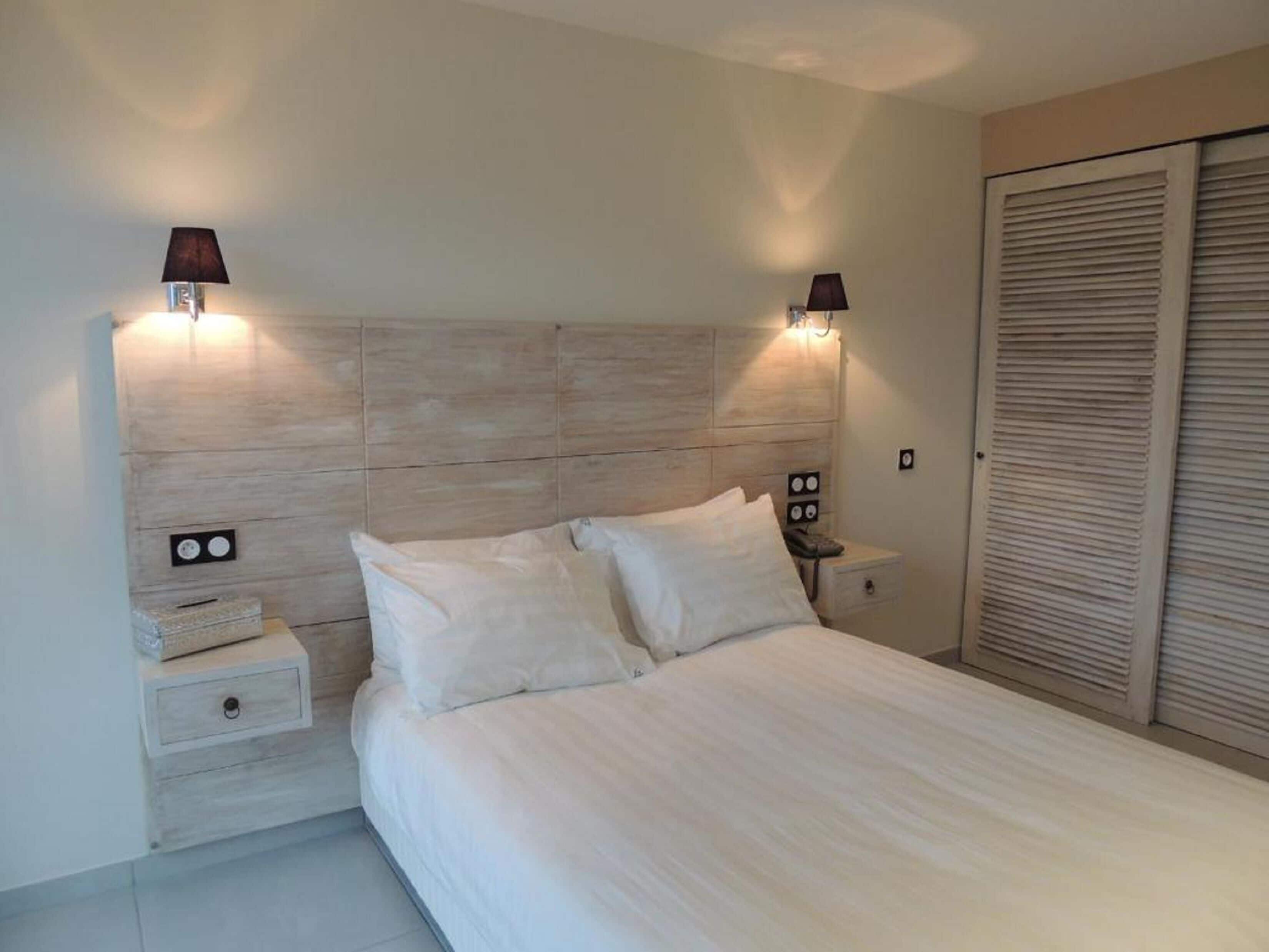 A bedroom with a wooden headboard, two bedside lamps, a nightstand, and a large closet.