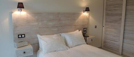 A bedroom with a wooden headboard, two bedside lamps, a nightstand, and a large closet.