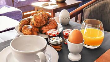 Una escena de desayuno con cruasanes, huevos y zumo de naranja sobre una mesa.