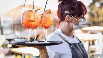 A person holding a tray with two glasses of orange beverage and a small bowl of olives.