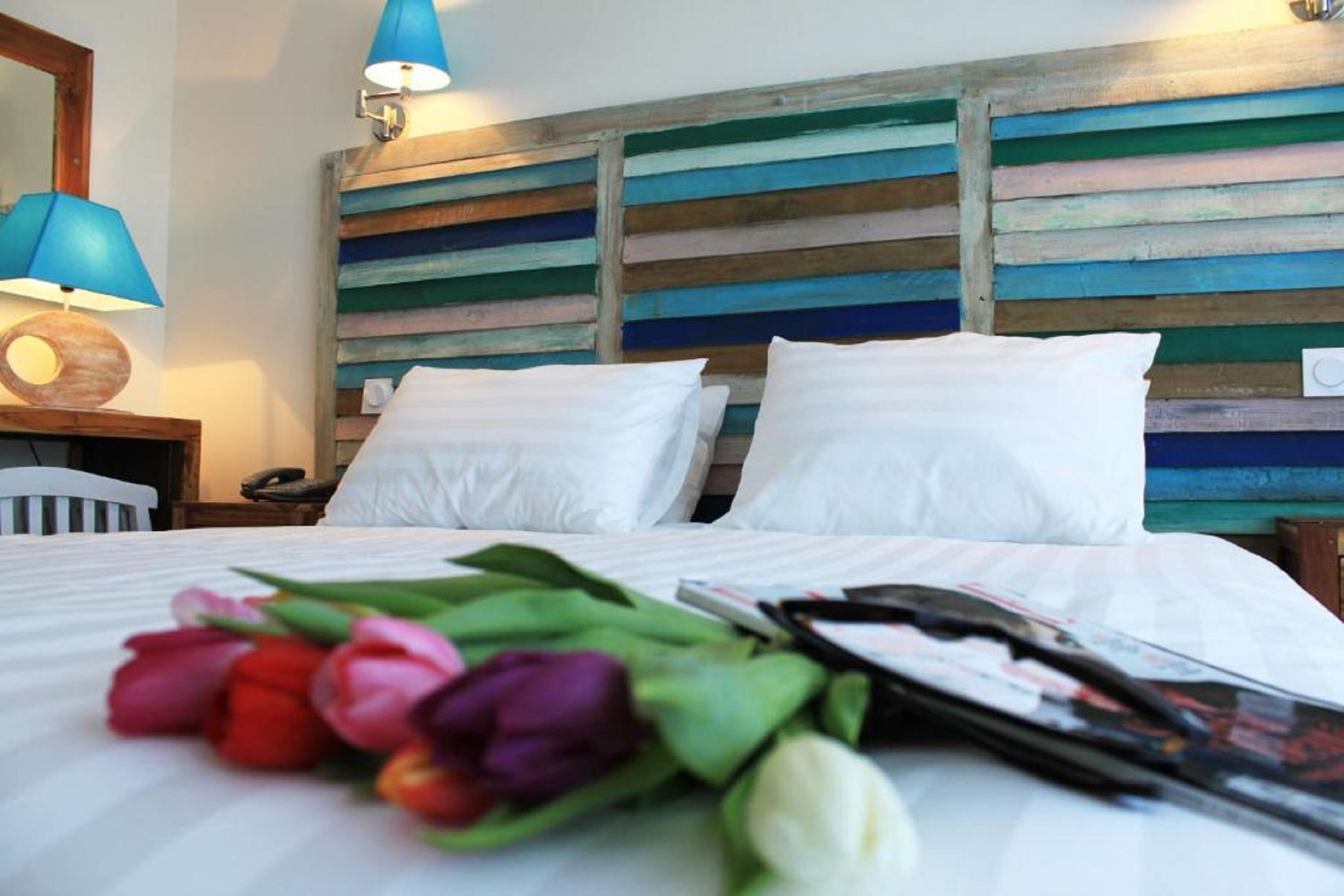 Una cama bien hecha con sábanas blancas, un cabecero de madera con rayas horizontales y un ramo de tulipanes sobre la cama.
