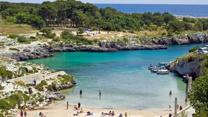 A coastal beach with clear turquoise waters, rocky terrain, and a forested area in the background. - Tenuta Pigliano (Bagnolo del Salento)