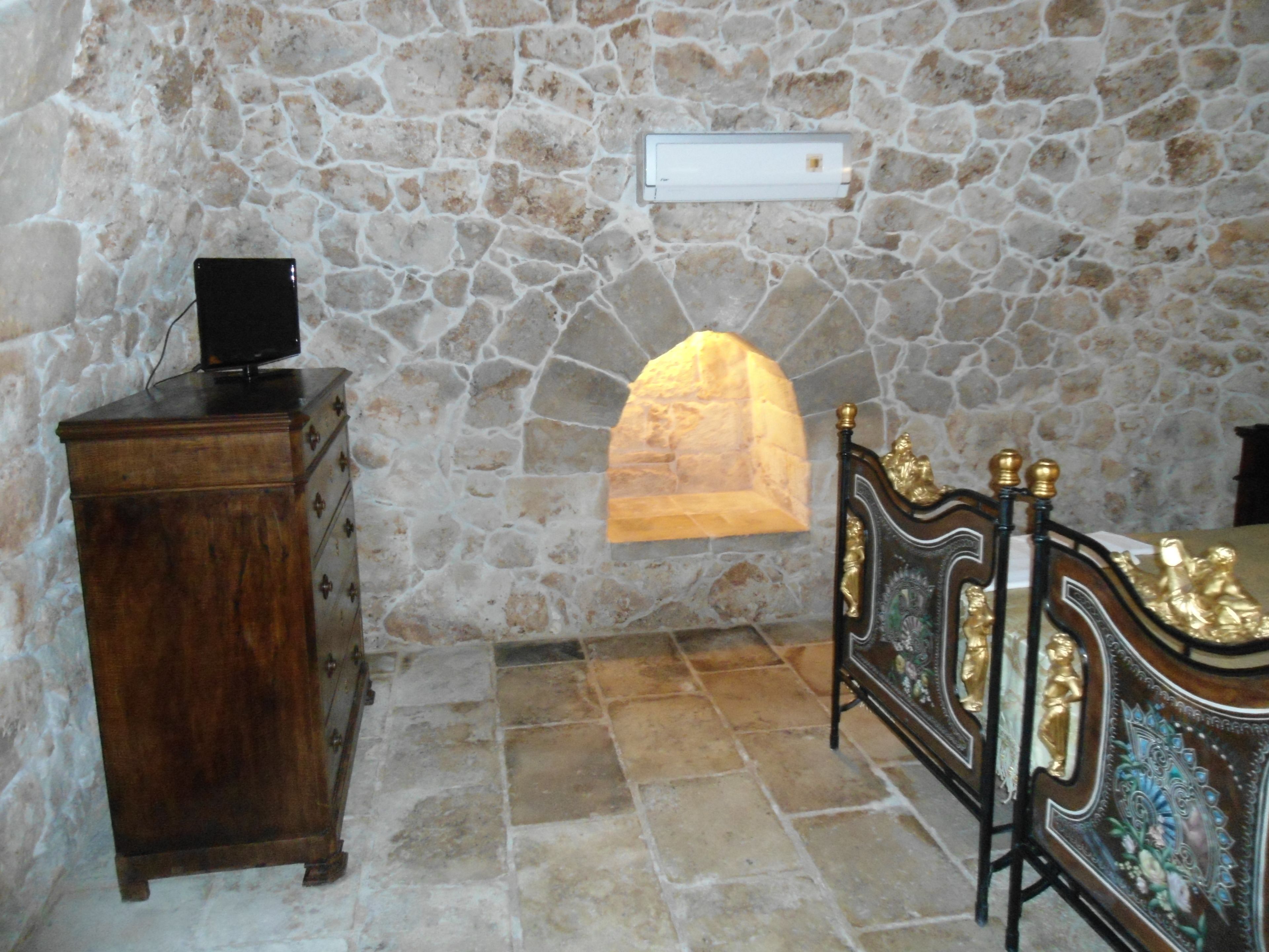 A stone-walled room with a bed, a dresser, and a stone fireplace.
