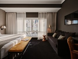 A hotel room with a bed, a sofa, a bench, and a TV mounted on the wall.