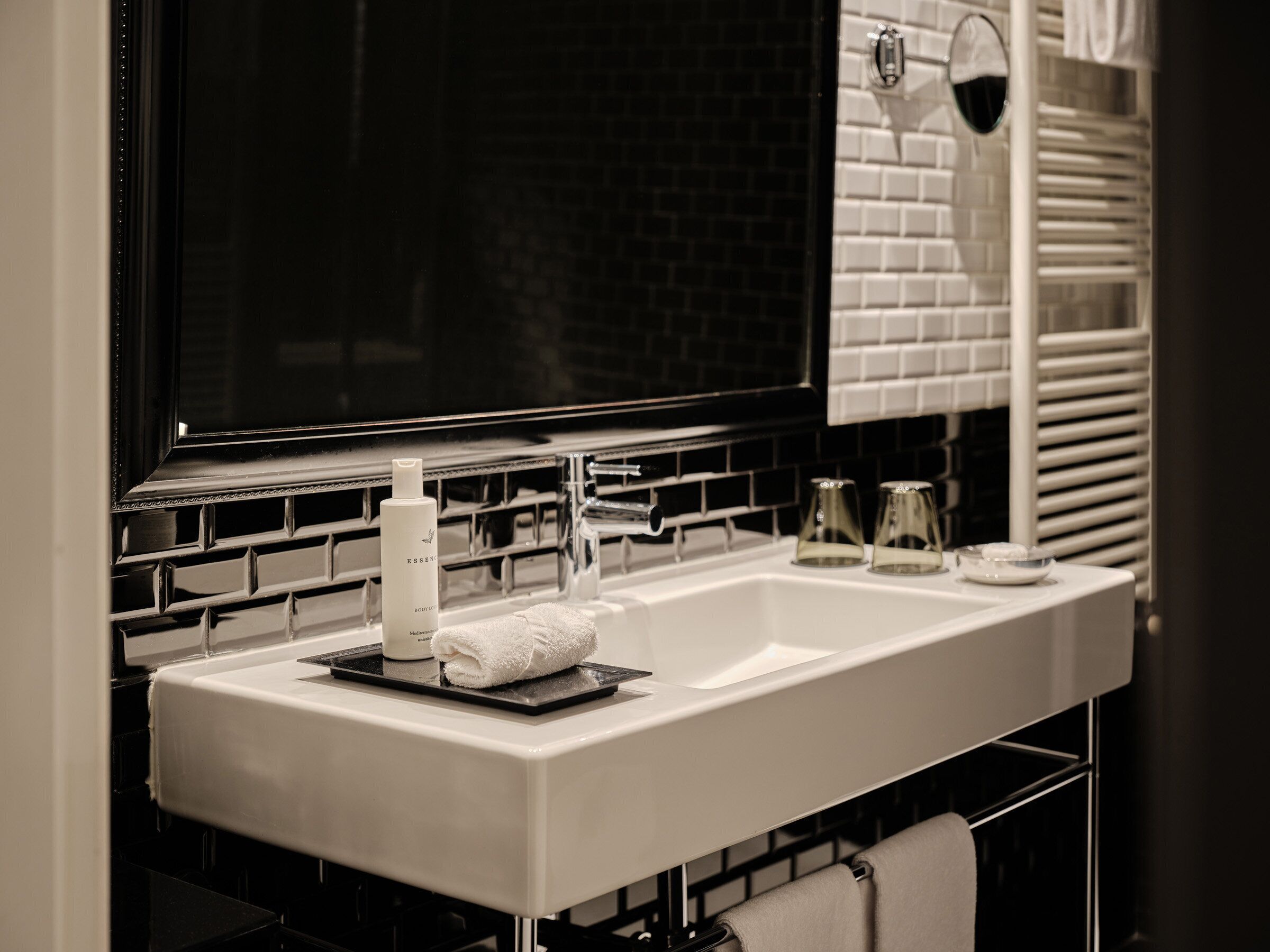Une salle de bain avec un lavabo blanc, un grand miroir et un mur recouvert de carreaux noirs.
