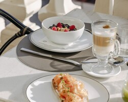 Ein Tisch gedeckt mit einer Schüssel Beeren und Nüssen, einer Kaffeetasse und einem Stück Lachs auf Toast.